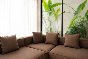 A brown sofa with cushions in a room with a window and large green plants. - Modern 2BR Private Pool Villa Near Pererenan Beach & Canggu (Badung)