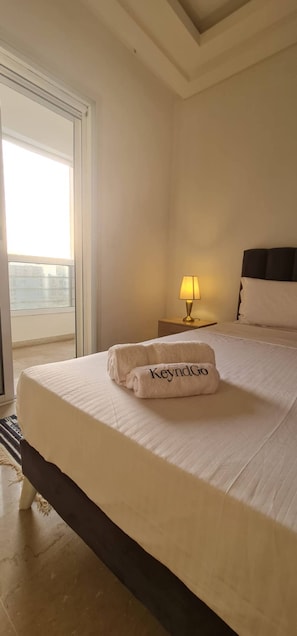 A hotel room with a bed, a nightstand with a lamp, a window, and a towel with 'KeyndGo' text. - Luxurious 3-Bedroom Apartment in Heart of Tunis (Tunis)