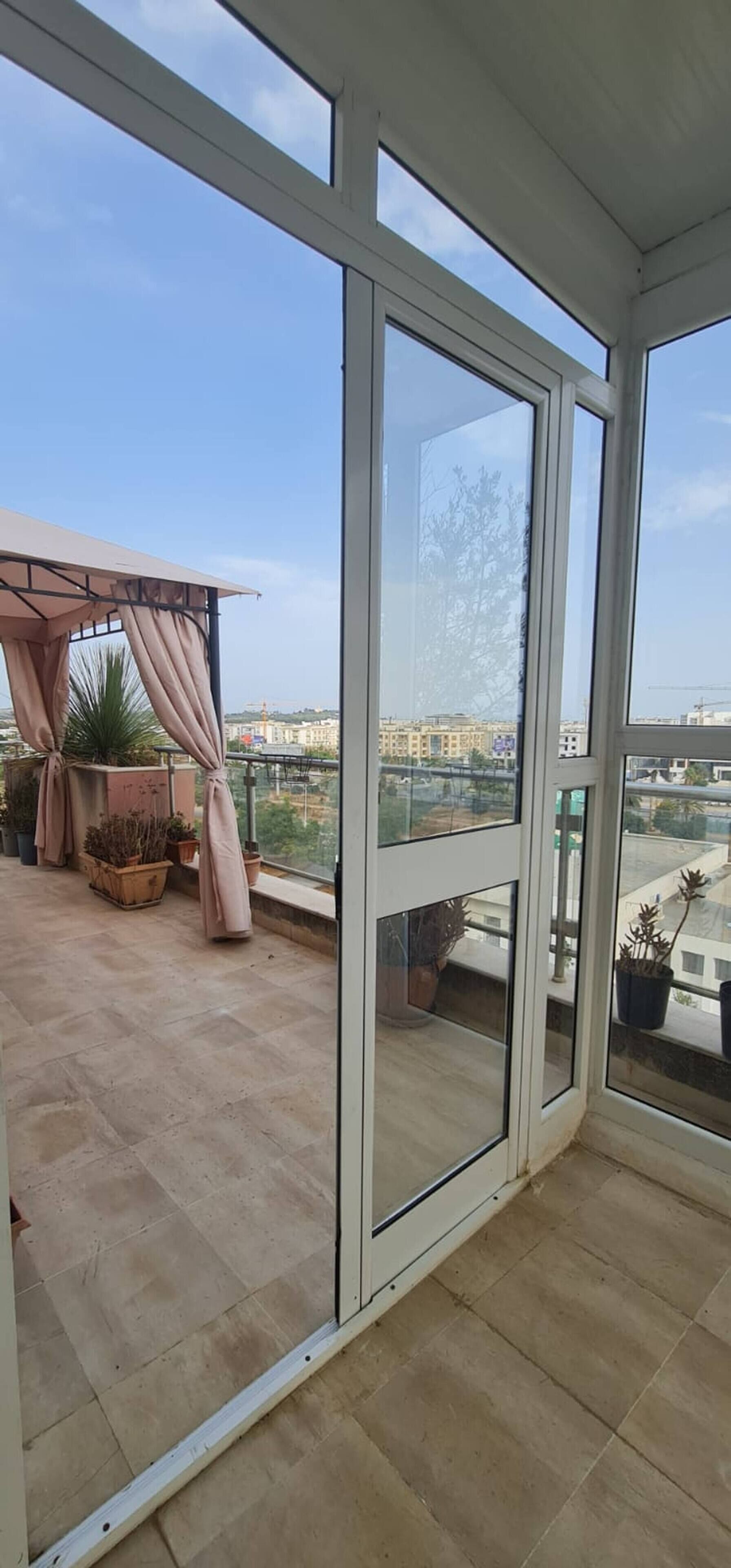 A balcony with a view of a cityscape, a pergola with curtains, and potted plants.