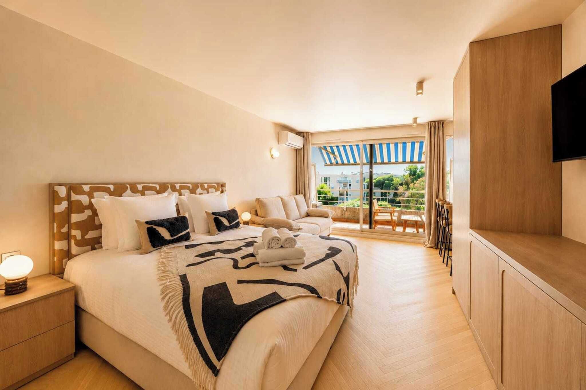 Una camera d'hotel con un letto grande, una televisione, un balcone con tenda a righe e pavimento in legno.