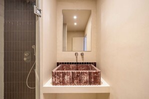Un baño con un lavamanos rectangular, un espejo encima y una zona de ducha a la izquierda.