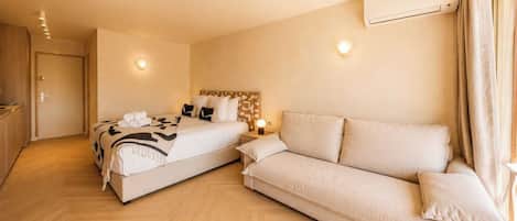 Et hotelværelse med seng, sofa, natbord, klimaanlæg og dør.