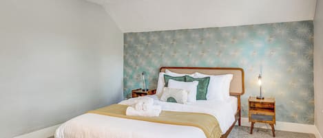 Een netjes opgemaakt bed met houten frame, een nachtkastje met lamp, en een bloemen behang wand.
