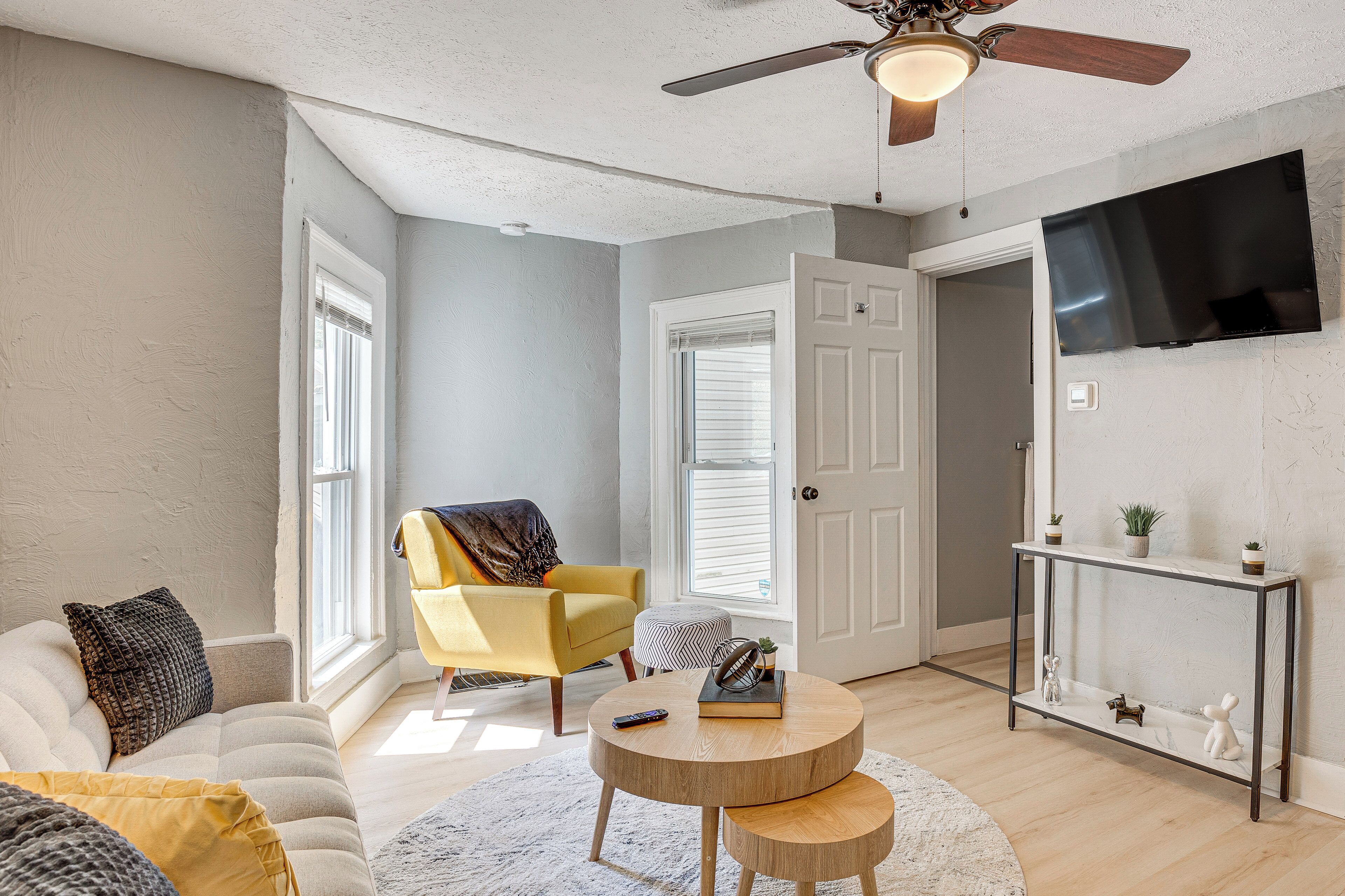 A living room with a sofa, armchair, round coffee table, and a TV mounted on the wall.