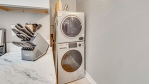 Uma cozinha compacta e moderna com máquina de lavar e secar integradas, eletrodomésticos de aço inoxidável e bancada de mármore.