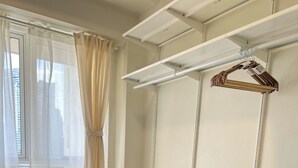 A bedroom with a bed, a wardrobe with shelves, and a window with curtains. - Nordic Nest Makati (Makati City)