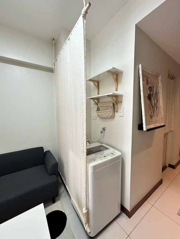 Habitación compacta con lavadora, sofá y cortina.