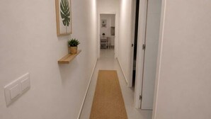 A hallway with a wooden shelf, a framed picture, and a woven rug leading to a room. - Salinas Home (Antigua)