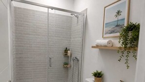 A modern bathroom with a glass-enclosed shower, a toilet, a sink, and a small shelf with toiletries. - Salinas Home (Antigua)