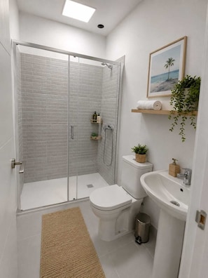 Ein modernes Badezimmer mit einer gläsernen Duschkabine, Toilette, Waschbecken und einer kleinen Ablage für Toilettenartikel.