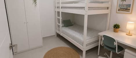 A bunk bed with a desk and chair, a small rug, a cabinet, and a plant on the wall.