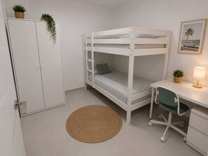 Ein Stockbett mit Schreibtisch und Stuhl, ein kleiner Teppich, ein Schrank und eine Pflanze an der Wand.
