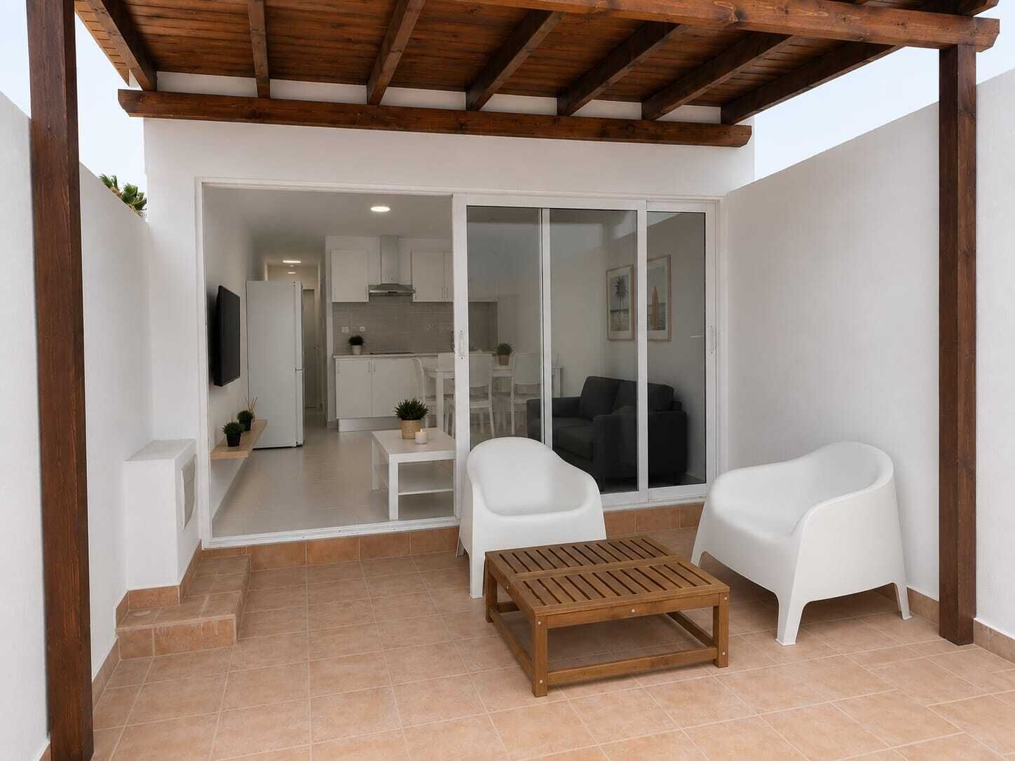 A modern living area with a wooden ceiling, white furniture, and a sliding glass door leading to a kitchen.