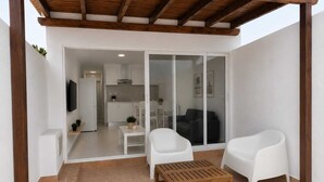 A modern living area with a wooden ceiling, white furniture, and a sliding glass door leading to a kitchen. - Salinas Home (Antigua)