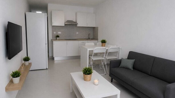 A modern living room with a grey sofa, a white coffee table, and a flat-screen TV mounted on the wall. - Salinas Home (Antigua)