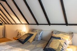Ein Schlafzimmer mit schrägem Dach, einem Bett mit gemusterten Betttextilien, einem Nachttisch und einer Lampe.
