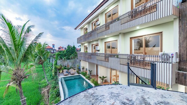 A multi-story residential building with balconies, a swimming pool, and lush greenery.