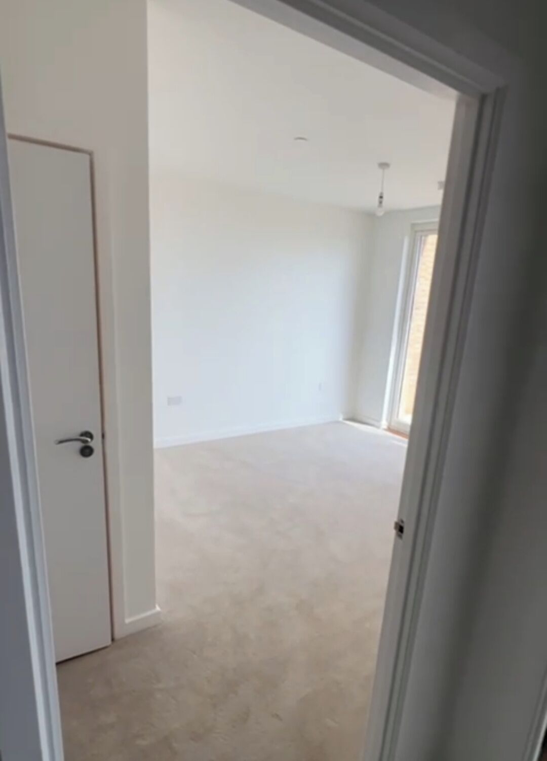 Une pièce avec une porte, un interrupteur et un luminaire au plafond.