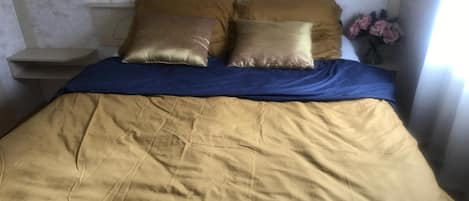 A bed with a blue bedspread and two gold pillows.