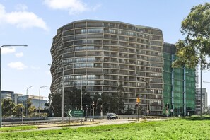 A modern building with a unique curved facade, surrounded by greenery and urban infrastructure. - Lake View 1-Bed Apartment Canberra Centre (Canberra)