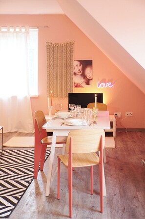 A dining area with a table set for two, a neon 'love' sign, and a window with curtains. - Just like home, but in a completely different place (Bengel)