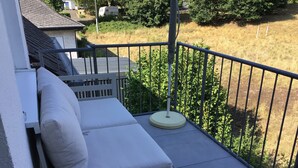 Ein Balkon mit einem einzelnen weißen Loungesessel und einem kleinen Tisch, umgeben von einem Metallgeländer.