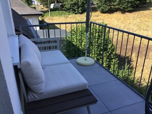 A balcony with a single white cushioned lounge chair and a small table, surrounded by a metal railing. - Just like home, but in a completely different place (Bengel)
