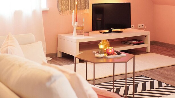 Ein modernes Wohnzimmer mit Flachbildfernseher, einem weißen Sofa, einem Couchtisch mit Dekoration und einem gemusterten Teppich.