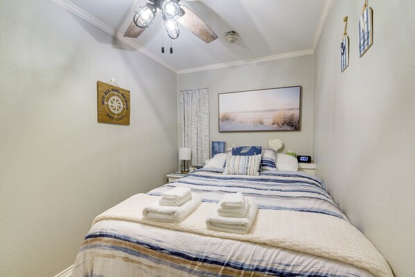 Een slaapkamer met een bed, een plafondventilator, een schilderij, een klok en een wanddecoratie.
