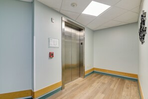 Een gang met houten vloer, een brandmelder en een lift.