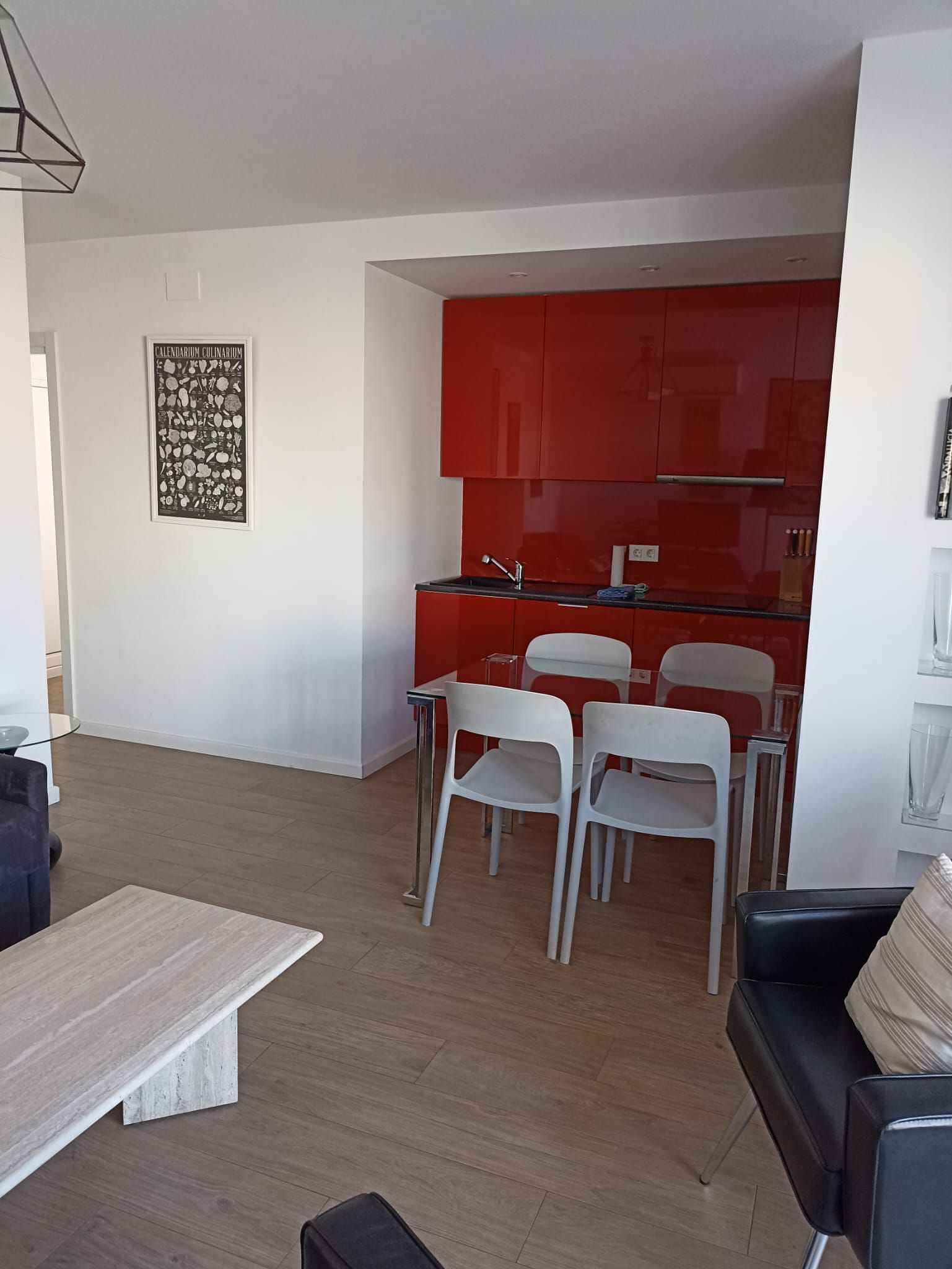 Een moderne keuken met rode kastjes, een glazen eettafel en witte stoelen.