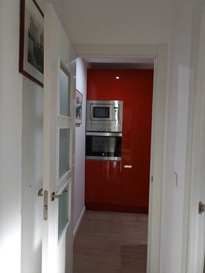 Ein schmaler Flur führt zu einer Küche mit einem roten Schrank und Edelstahlgeräten.