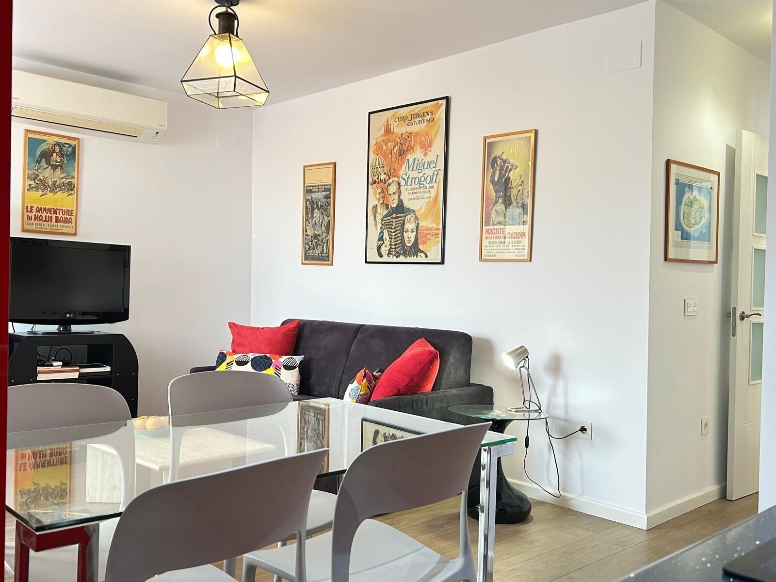 A modern living room with a sofa, a dining table with chairs, a TV, and framed posters on the wall.