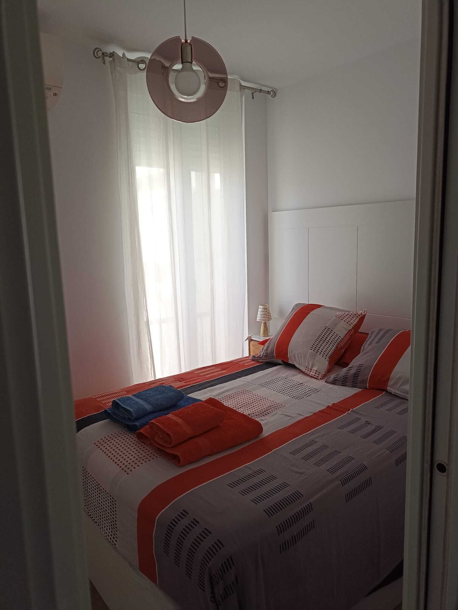 Un dormitorio con cama, mesita de noche, lámpara y ventana con cortinas.