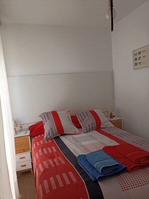 Ein ordentlich bezogenes Bett mit einem gestreiften Bettüberwurf und Kissen, ein Nachttisch mit Lampe sowie ein an der Wand hängendes Kunstwerk.