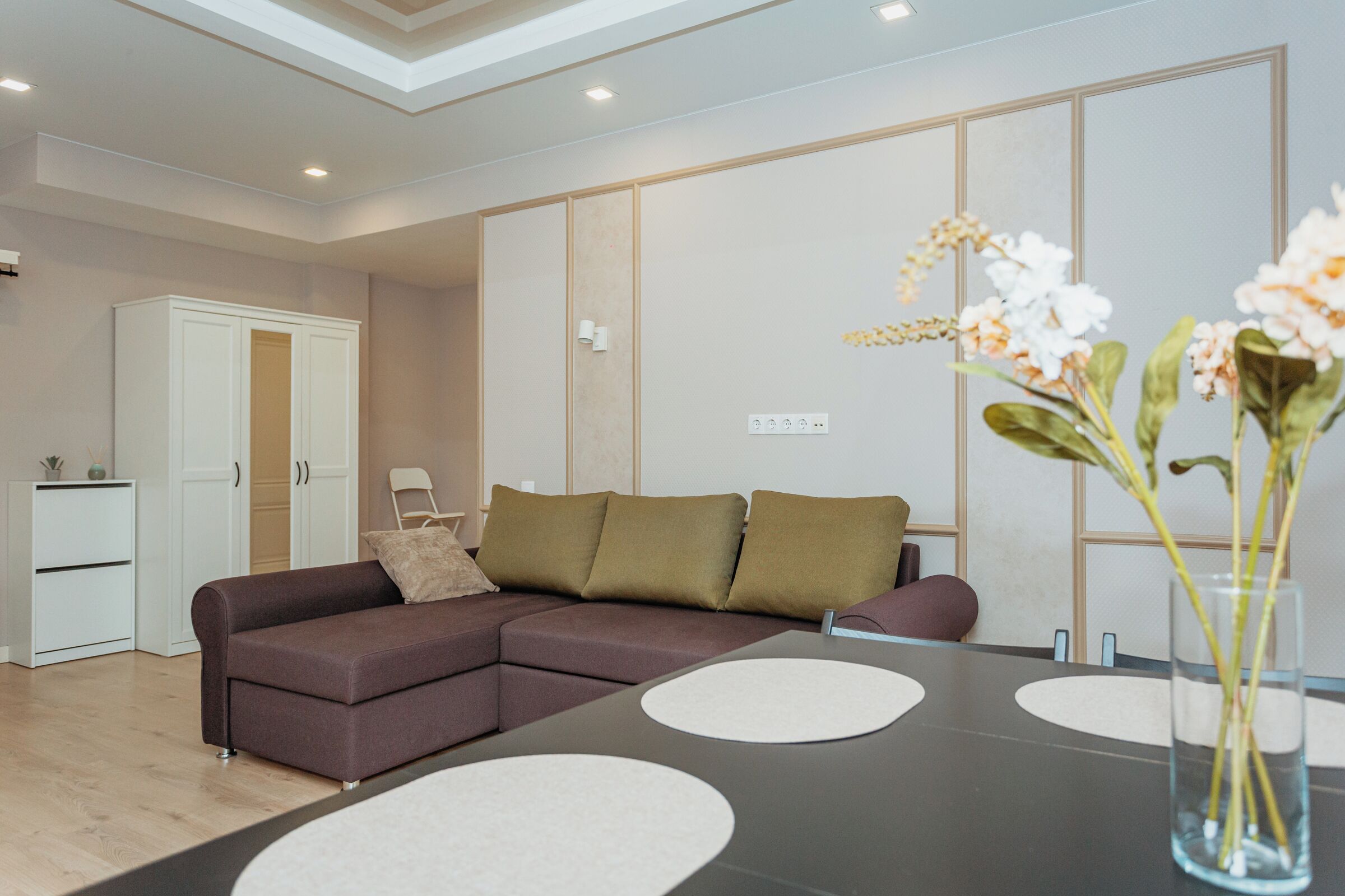 A modern living room with a brown sofa, a glass coffee table, and a vase with flowers.