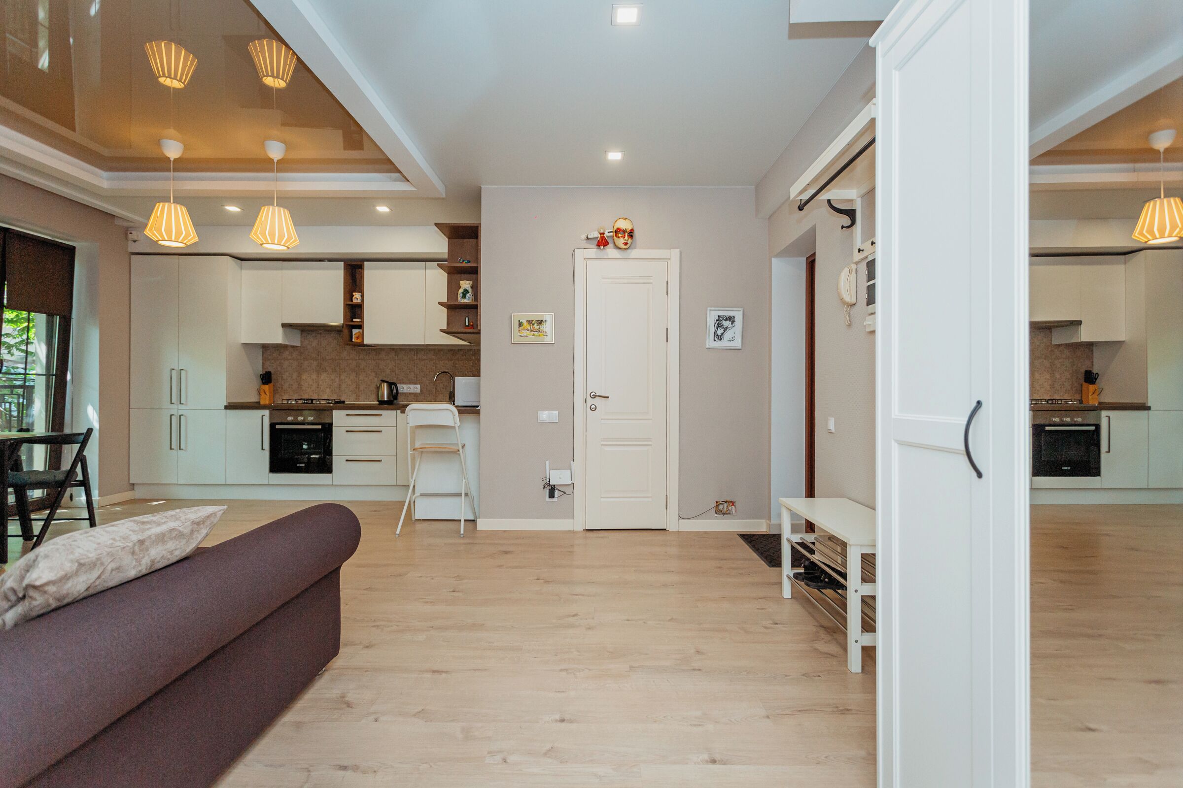 A modern kitchen with white cabinets, a dining area with a sofa, and a hallway leading to another room.
