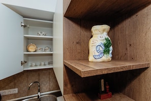 Uma cozinha com uma prateleira de madeira que contém um vaso de cerâmica e um termômetro.
