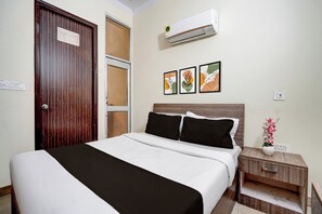 Un dormitorio con cama, mesita de noche, aire acondicionado de pared y tres cuadros enmarcados.