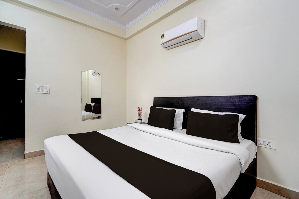 A hotel room with a bed, a nightstand, a mirror, an air conditioning unit, and a door.