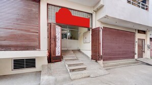 Un edificio con toldo rojo, un conjunto de escalones de hormigón que llevan a una puerta con un panel decorativo, y un portón de garaje.