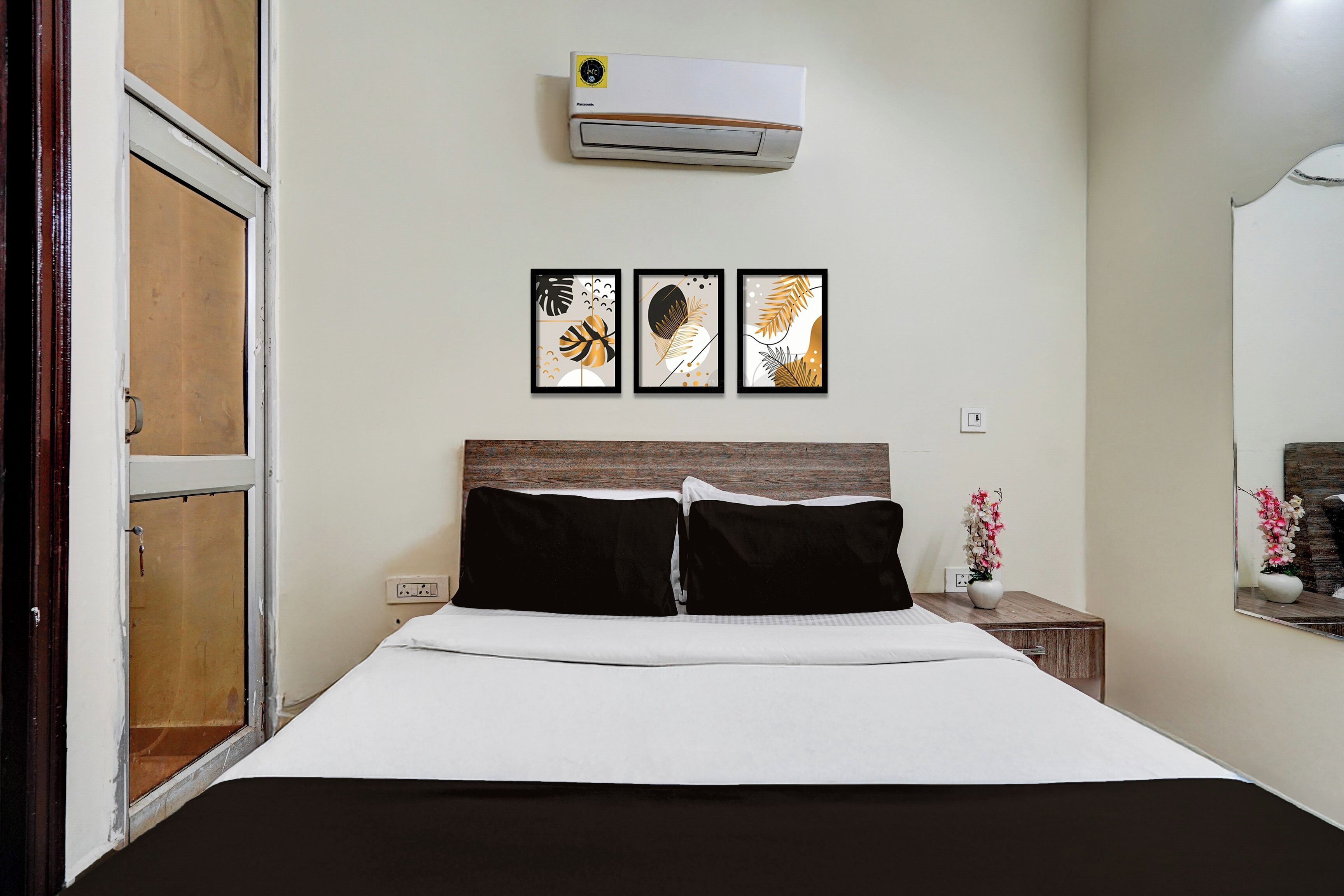 A hotel room with a bed, a wall-mounted air conditioner, and three framed artworks above the bed.