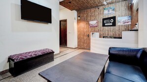 Zona de recepción de un hotel con televisor de pantalla plana, mostrador de recepción, sofá y banco.