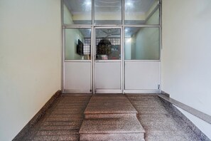 A set of double doors with a glass panel, leading to a room with a ceiling fan and a television. - Hotel O Railway Station Road Formerly (Alwar)