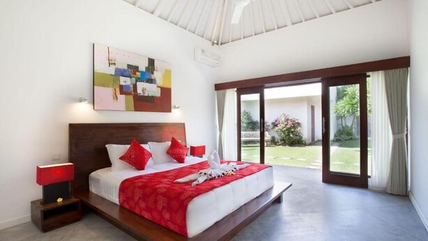 Habitación de hotel con una cama grande, una pared de acento roja, un ventilador de techo y vistas al jardín a través de la puerta corrediza de vidrio.