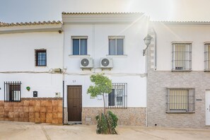 A two-story building with a tiled facade, numbered 57, featuring a central door, two windows with barred windows, and an air conditioning unit. - The Foosball House: Full House in the ChillOut Village, Pool, Views (Villanueva del Rosario)