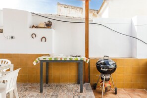 Un patio con tavolo, sedie, una griglia per barbecue e pavimento piastrellato.