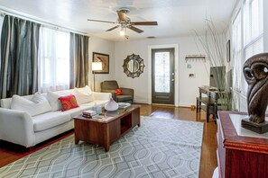 A living room with a white sofa, a coffee table, a ceiling fan, and a door with a decorative glass panel. - Walk to Shops & Restaurants! NOLA Extended Stay (New Orleans)
