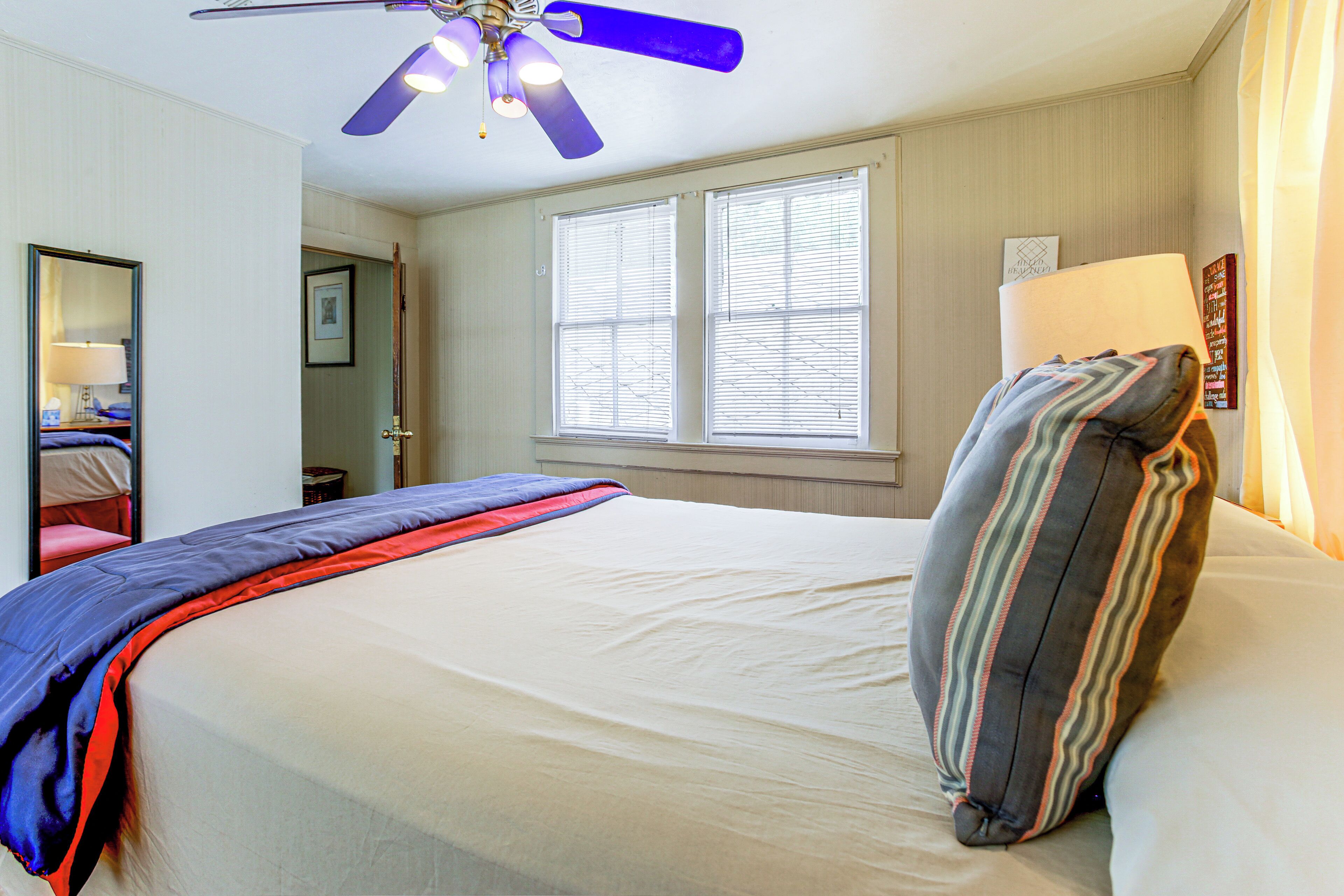 A hotel room with a bed, a ceiling fan, a window with blinds, a bedside lamp, and a wall-mounted sign.