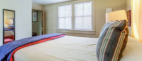 Ein Hotelzimmer mit Bett, Deckenventilator, Fenster mit Jalousien, Nachttischlampe und einem an der Wand befestigten Schild.